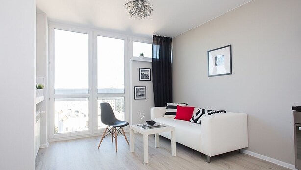 Una sala de estar moderna con un sofá blanco, una silla negra, una mesita y un ventanal con cortinas.