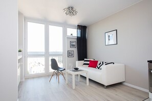En moderne stue med en hvid sofa, en sort lænestol, et lille bord og et stort vindue med gardiner.