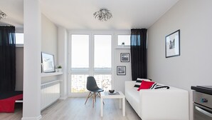 Un salón moderno con un sofá blanco, una silla negra, una mesita y vistas a la ciudad a través de grandes ventanales.