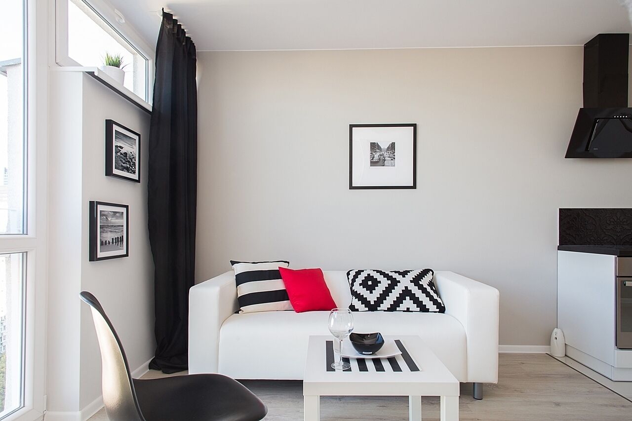A modern living room with a white sofa, black and red cushions, a glass coffee table, and framed pictures on the wall.