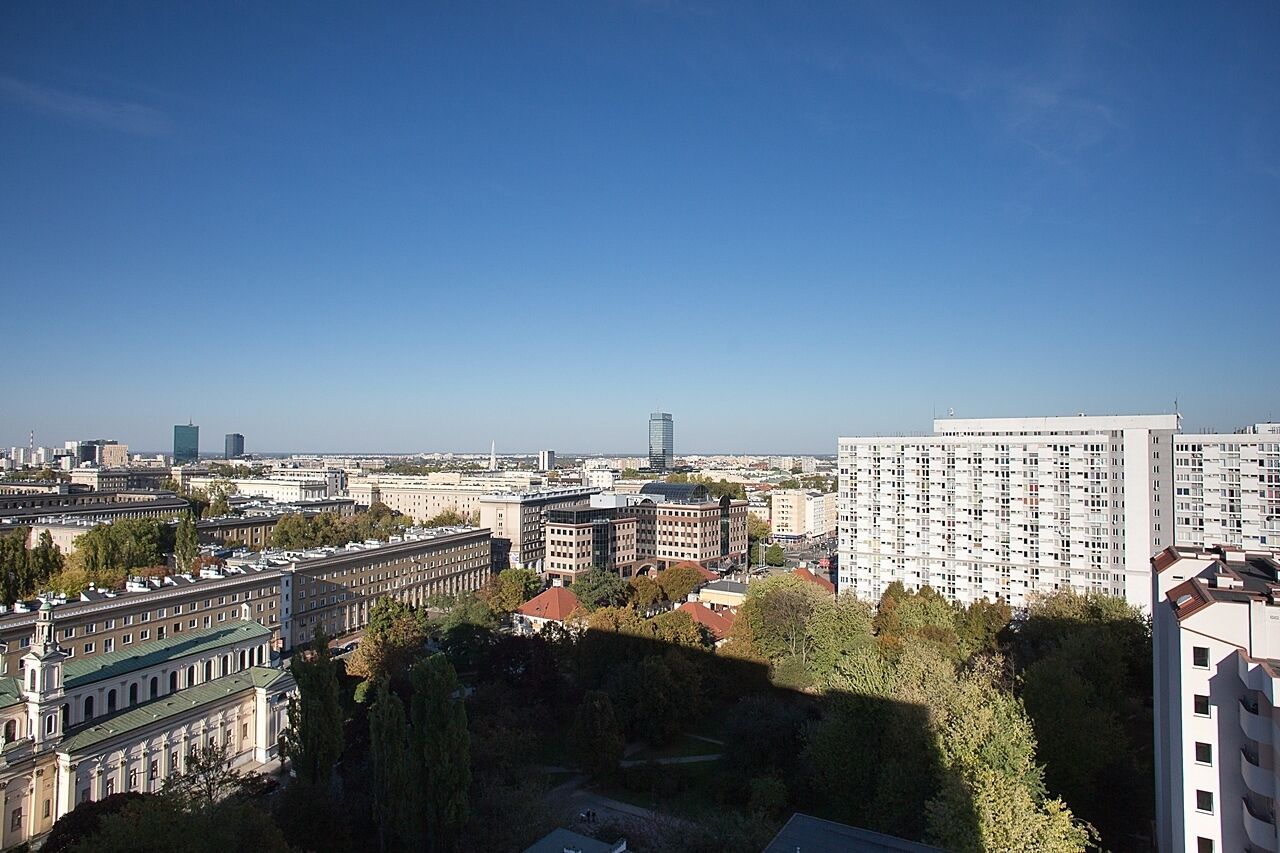 A cityscape with a mix of modern and historic buildings, including a prominent high-rise and a large, classical building with a green roof.