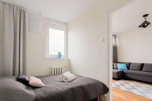 Un dormitorio ordenado con cama, un sofá gris y una ventana con cortinas.