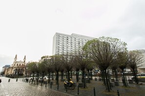 Un área pavimentada con árboles, un scooter estacionado y un edificio con una torre de reloj.