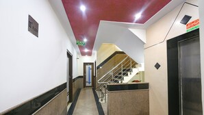 Un couloir avec un plafond rouge, un panneau indiquant le troisième étage, un panneau de sortie et un escalier menant à un ascenseur.