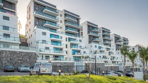 A modern multi-story residential building with balconies, a stone facade, and a parking area with cars. - Morocco Mini Penthouse W Panoramic Views (Tiberias)