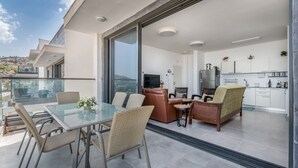 A modern apartment with a balcony, a dining area with glass-top table and wicker chairs, a living area with leather sofas, and a kitchen with white cabinets and a refrigerator. - Morocco Mini Penthouse W Panoramic Views (Tiberias)