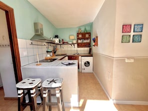 A kitchen with a microwave, stove, and washing machine. There are two stools with starfish designs. - La Chumbera high rent ideal for couples (San José)