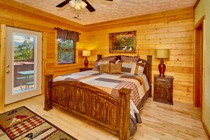 Une chambre dans une cabane en bois, avec un lit, deux tables de chevet, un ventilateur de plafond et une fenêtre avec des stores.