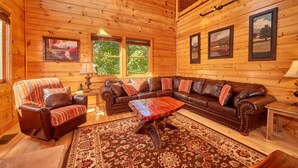 L’intérieur chaleureux d’un chalet avec un canapé en cuir, un fauteuil à motifs, une table basse en bois et un grand tapis.