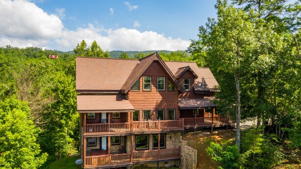 Une cabane en rondins à deux étages, dotée d’un balcon, entourée d’une végétation luxuriante et avec une chaîne de montagnes en toile de fond.