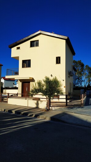 A two-story building with a flat roof, a small balcony, and a tree in front.