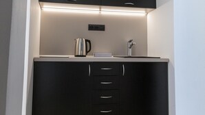 A compact kitchen with black cabinets, a stainless steel kettle, and a built-in air conditioner. - Golden Apartments (Kosice)
