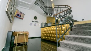 A reception area with a staircase, a reception desk, and a wall clock. - Golden Apartments (Kosice)