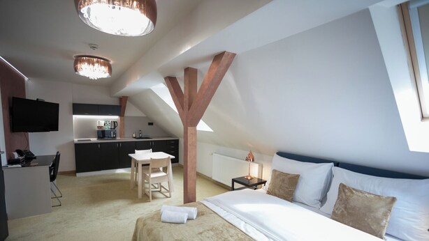 A bedroom with a large bed, a desk, and a kitchenette. - Golden Apartments (Kosice)