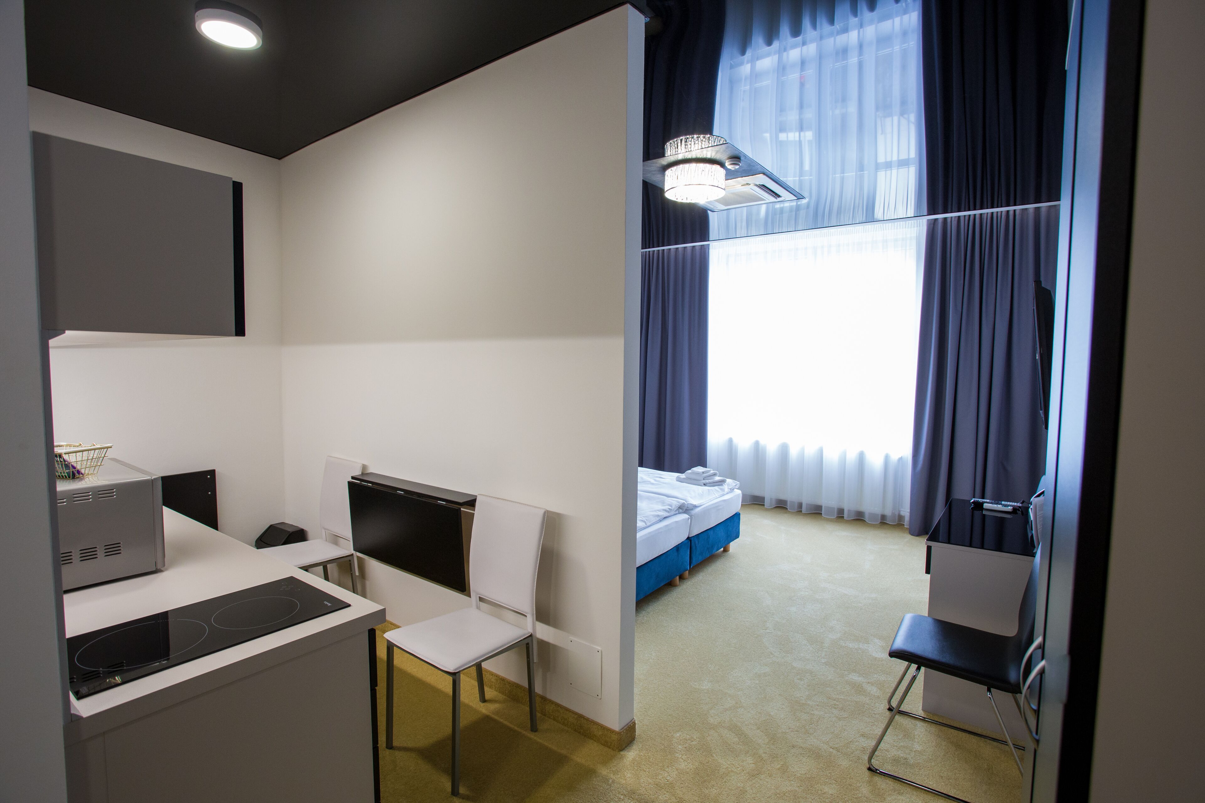 A hotel room with a kitchenette, a bed, a desk, and a chair.