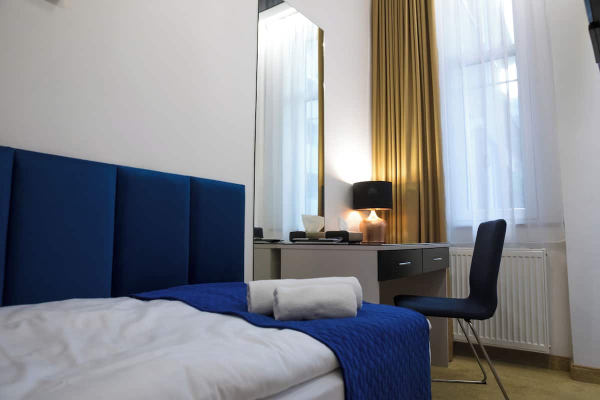 A hotel room with a bed, a desk, a chair, a lamp, and a window with curtains.