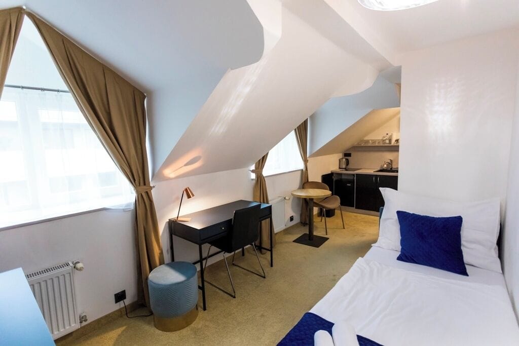 Een kleine hotelkamer met een bed, bureau, stoel en kitchenette.