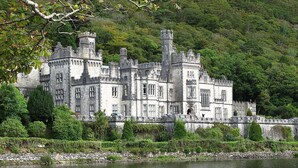 Un grand bâtiment historique en pierre, doté de nombreuses tours et tourelles, situé au bord d’un plan d’eau.