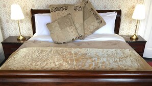 Un lit bien fait, recouvert d’une couvre-lit à motifs et agrémenté de deux coussins décoratifs, avec deux tables de chevet de chaque côté, sur lesquelles sont posées des lampes.