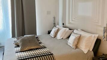 A modern bedroom with a large bed, a headboard with a geometric pattern, a bedside table with a lamp, and a window with curtains.