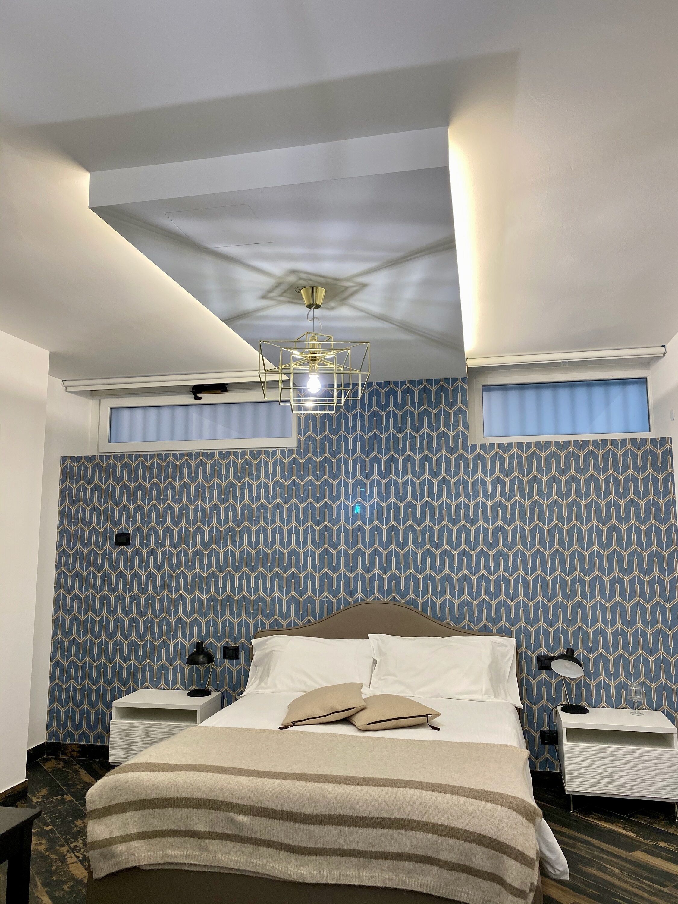 Ein Hotelzimmer mit Bett, Nachttischen, einer Deckenleuchte und ornamentalem Wandpapier.