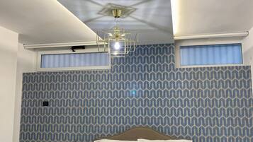 Ein Hotelzimmer mit Bett, Nachttischen, einer Deckenleuchte und ornamentalem Wandpapier.