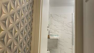 A hallway with a geometric patterned wall, a marble-tiled bathroom, and a modern light fixture.