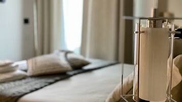A neatly made bed with a white duvet, a grey throw, and a metal bedside table with a lamp.
