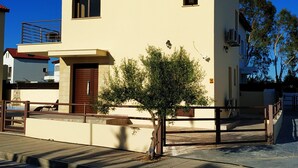 Un edificio de dos pisos con techo plano, un pequeño balcón y un árbol enfrente.