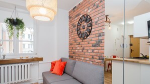 Ein modernes Wohnzimmer mit grauem Sofa, einem roten Kissen, einer Ziegelwand und einer großen Uhr.