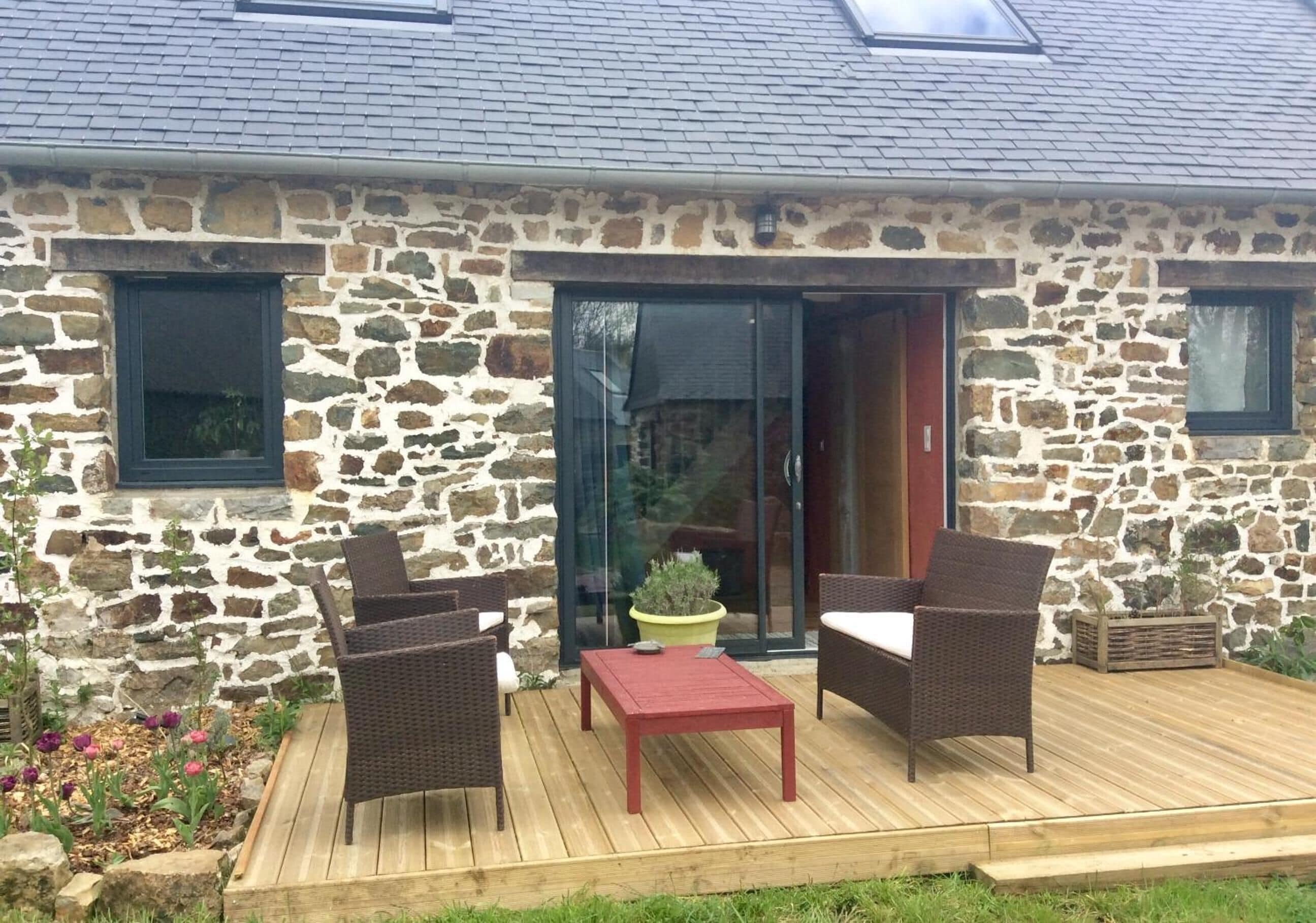 A stone building with a wooden deck, wicker furniture, and a potted plant.