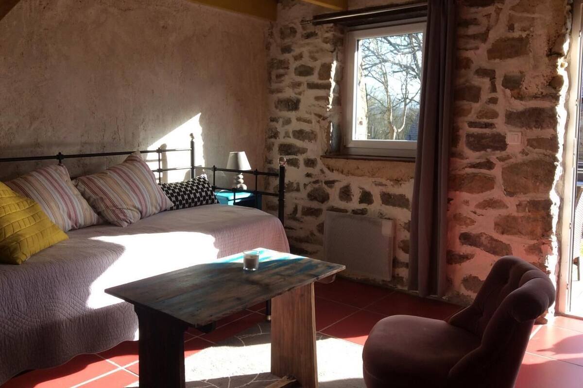 A cozy room with a bed, a table, and a chair. There is a window with a view of trees outside.