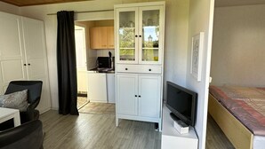 A compact room with a wooden ceiling, a bed, a TV, a desk, and a kitchen area. - Holiday house in a quiet location and near the forest (Wernigerode)
