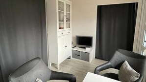 A modern living room with two black leather armchairs, a white coffee table, and a television on a white stand. - Holiday house in a quiet location and near the forest (Wernigerode)