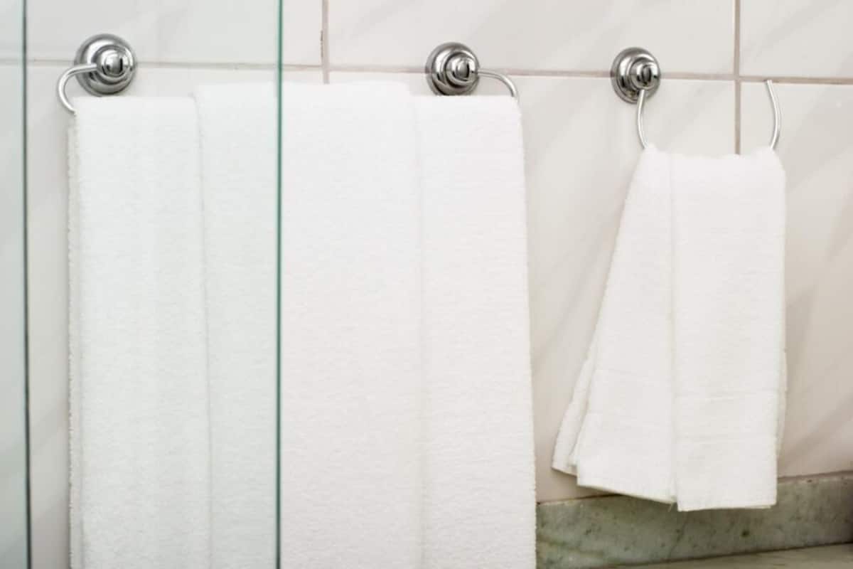 A bathroom with three white towels hanging on a rack against a tiled wall.