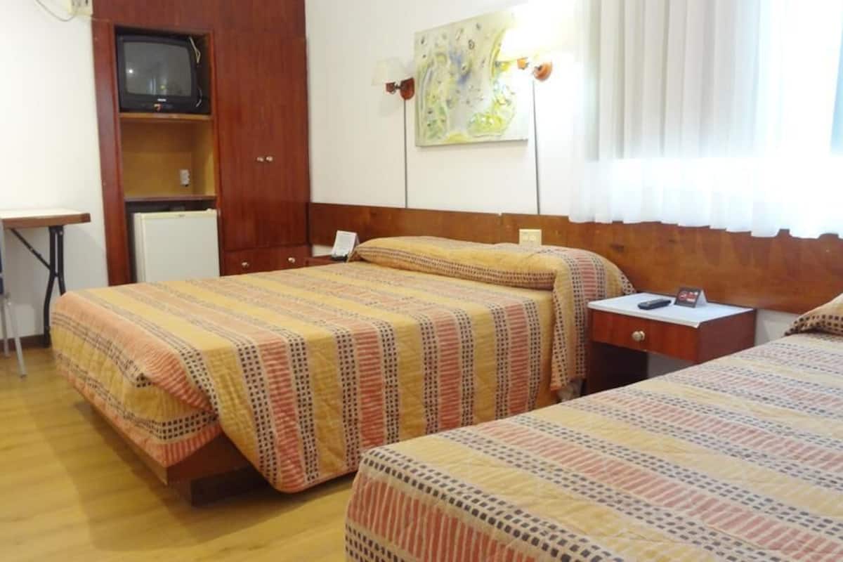 A hotel room with two beds, a desk, a chair, a television, and a painting on the wall.