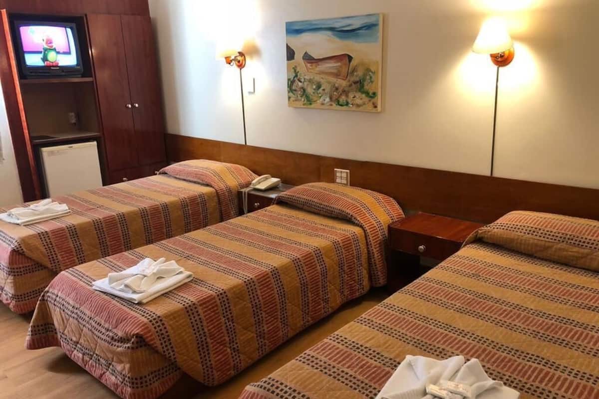 A hotel room with two single beds, a TV, a painting, and a lamp.