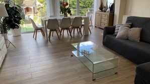 Ein modernes Wohnzimmer mit einem Glastisch, einem dunklen Sofa und einem Essbereich mit Stühlen und einem Tisch.
