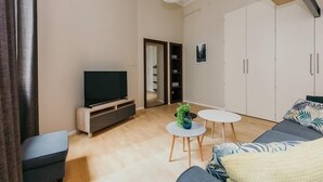 A modern living room with a flat-screen TV, a sofa, two small round tables, and a large wardrobe. - Apartment Cohen - Aleje Ujazdowskie (Warsaw)