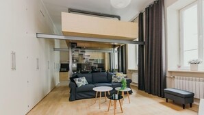 A modern apartment with a loft-style living area, a kitchen in the background, and a large window with curtains. - Apartment Cohen - Aleje Ujazdowskie (Warsaw)