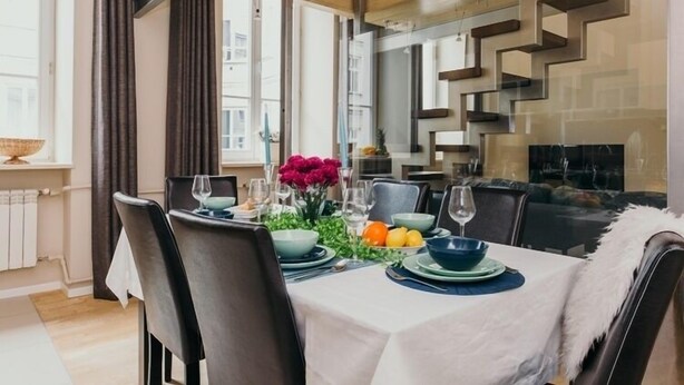 A modern dining area with a table set for four, featuring a white tablecloth, dark chairs, and a decorative centerpiece with flowers and fruits. - Apartment Cohen - Aleje Ujazdowskie (Warsaw)