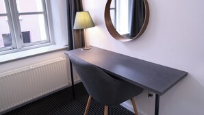 Une chambre moderne équipée d’un bureau, d’une lampe, d’un miroir rond et d’une fenêtre avec des rideaux.