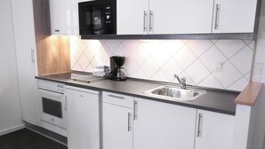 Une cuisine moderne avec des meubles blancs, un micro-ondes noir, une machine à café et un évier en acier inoxydable.
