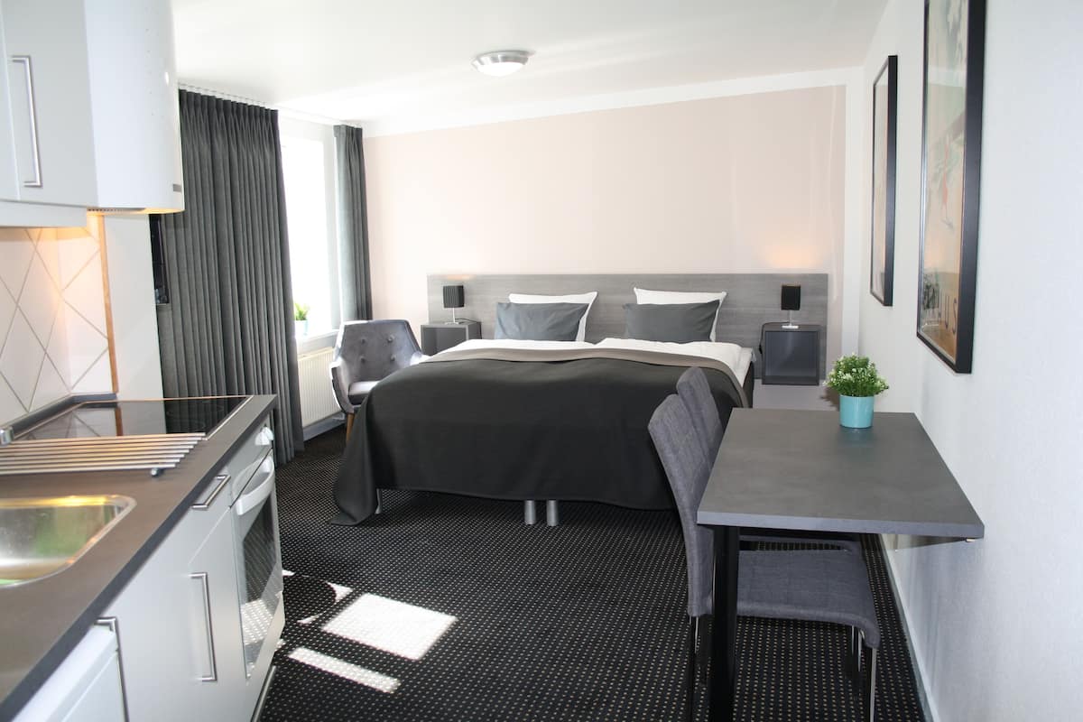 Een moderne hotelkamer met een bed, nachtkastjes, een klein bureau en een kitchenette.