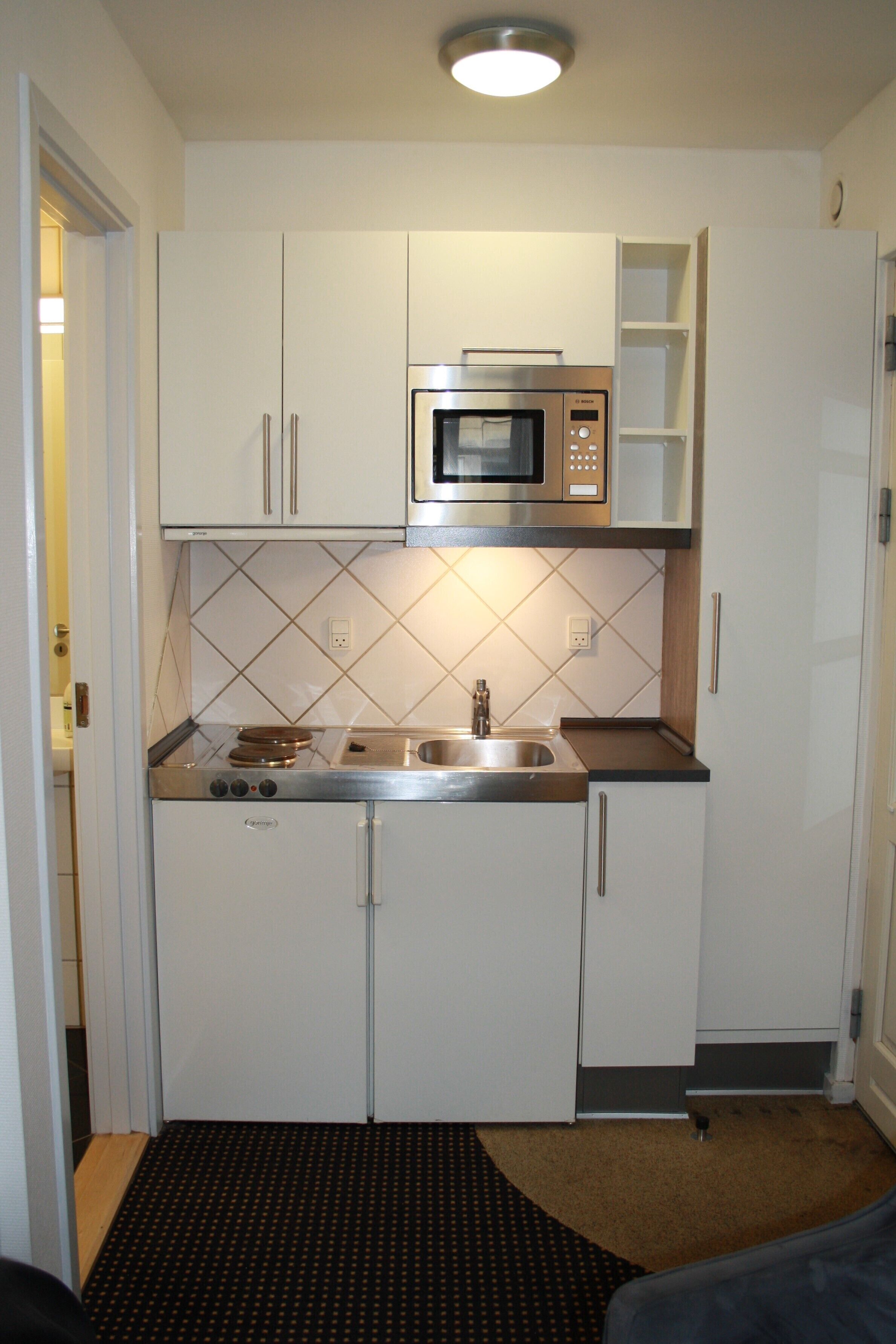Cocina compacta con armarios blancos, microondas integrado, pileta y estufa.