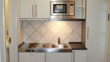 Cocina compacta con armarios blancos, microondas integrado, pileta y estufa.