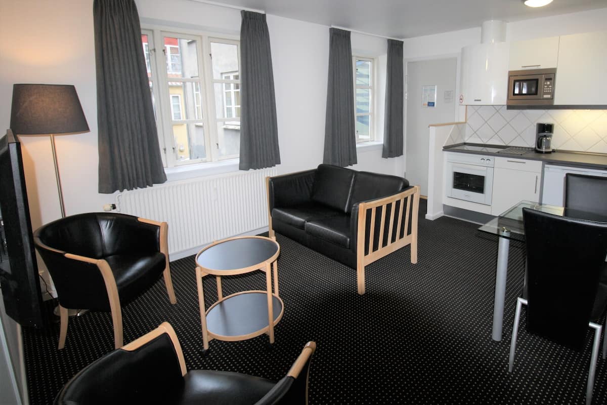 Een compacte hotelkamer met een kitchenette, een bank, een klein rond tafeltje en twee stoelen.