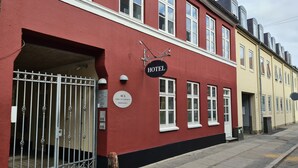Un bâtiment rouge avec une enseigne indiquant qu’il s’agit d’un hôtel. Il possède de nombreuses fenêtres et une grille ornée de motifs en métal.