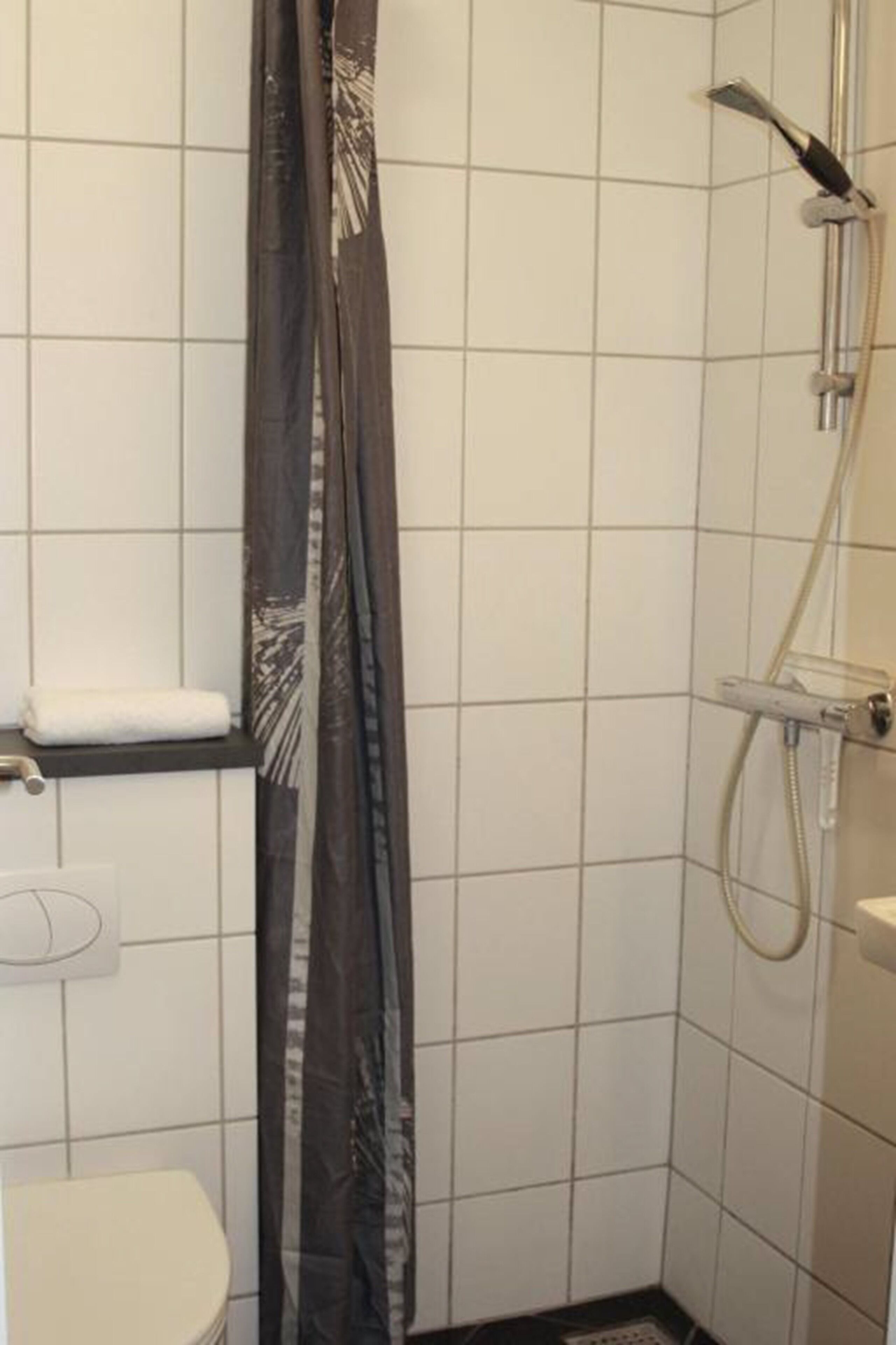 Un baño pequeño con inodoro, ducha y perchero para toallas.