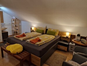 A cozy bedroom with a bed, bedside tables, a lamp, a coffee maker, and a small wooden bench. - Rosy's House Pension Privatzimmer (Bad Goisern)